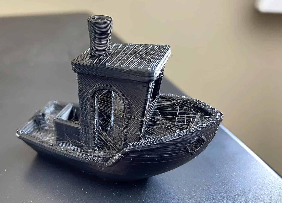 A 3D Benchy printed in wet PETG showing heavy stringing