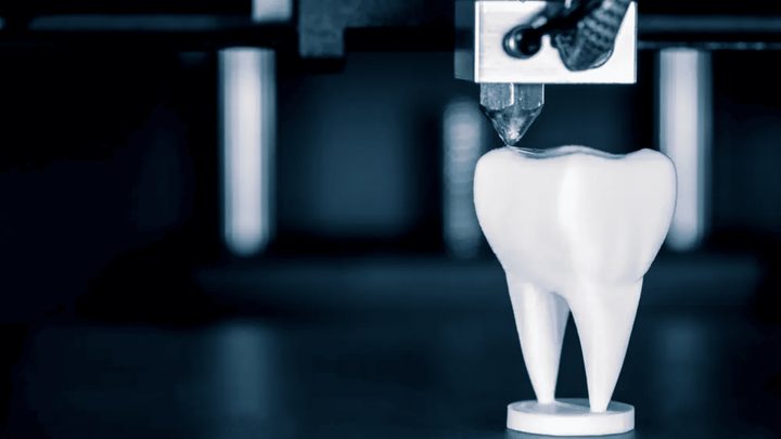 A 3D printed tooth model beside a resin printer